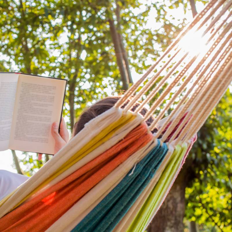 Personne allongée dans un hamac dans la forêt et lisant un livre - Réserver un hébergement insolite