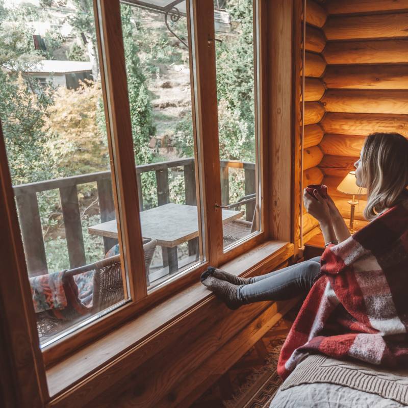 Femme assise sur un lit regardant par la fenêtre - Réserver un hébergement insolite