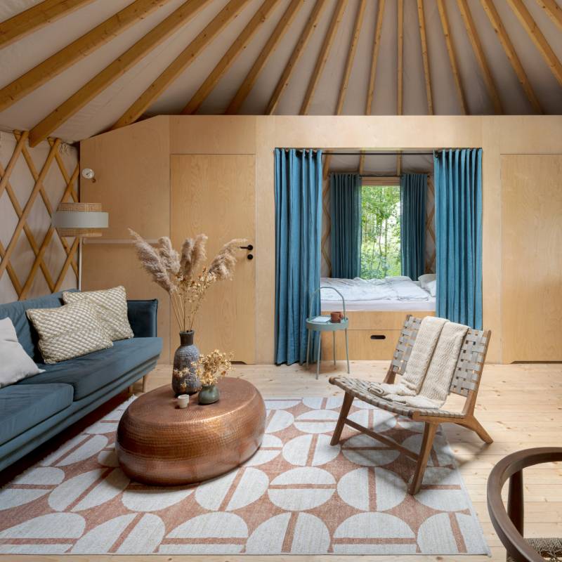 Intérieur de la yourte avec chambre fermée par un rideau, salon avec canapé et fauteuil cosy